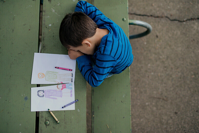 Auf Bank sitzendes Kind mit selbstgezeichneten Kinderbildern